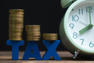 Time to pay TAX concept. TAX alphabet with stack of coin and vintage alarm clock on wooden working table in dark background, business and financial concept.