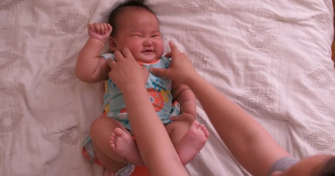 Asian mother is tickling her baby girl on the white bed as she haves fun