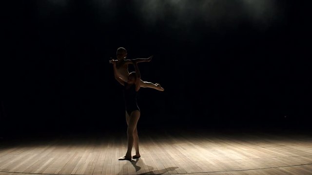 Two girls of the dancer make a complex gymnastic exercise on stage in the dark. Ballet. Complex dance support in the performance of two young children.