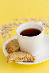 Gluten free homemade oats oatmeal cookies and cup of tea or coffee espresso on pastel yellow background. Copy space.