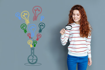 Scientific experiment. Cheerful diligent student feeling curious while looking through the magnifying glass in a modern laboratory