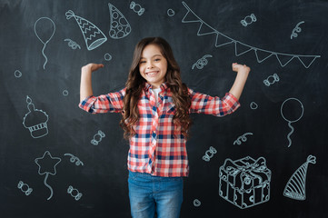 Happy birthday. Positive little girl smiling and putting her hands up while having a wonderful birthday party