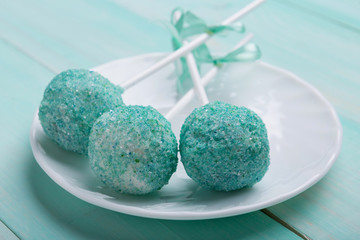three turquoise cake pop in sugar on a white plate, on turquoise boards