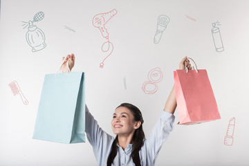 Loving shopping. Cheerful emotional young woman looking excited and putting her paper bags up while...