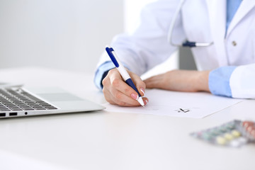 Female doctor filling up prescription form while sitting at the desk in hospital closeup. ...