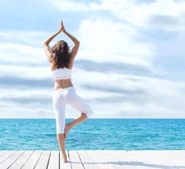  Attractive woman in white sporty clothes doing yoga on a wooden pier. Yoga, sport, leisure, recreation and freedom. © Acronym