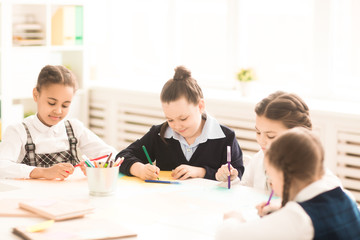 Group of schoolgirls draw with crayons together at the table