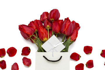 Red tulips in a paper gift bag, gift and scattered petals of tulips on a white background. Top View.