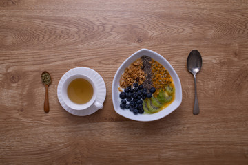 A glass of hot tea put with a dish of breakfast, cereal and dried fruit yogurt on brown wood texture table.