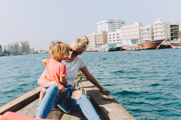 Fototapeta na wymiar Young beautiful woman with her little son sitting at boat and contemplating the seascape of Dubai