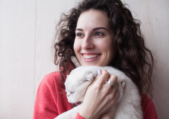Beautiful young woman holding white Scottish fold kitten. Family concept. Woman with curly hair with cat at home.