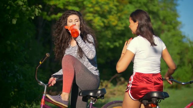 Rest on a bike ride, two female cyclists drink water and talk , sunny summer day