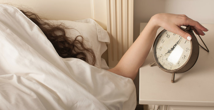 Young woman reach out one's hand Press the button to turn off the alarm clock in morning