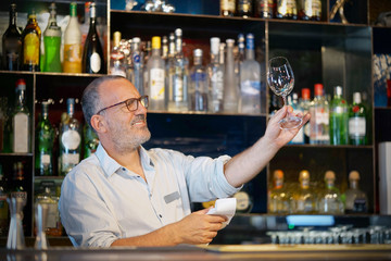 Elderly bartender cleans the glass. A handsome bartender polishes a glass of wine glasses. The concept of service.