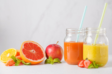 Fototapeta na wymiar Multicolored summer fruit juices or smoothie in glass jars and ingredients on white table.