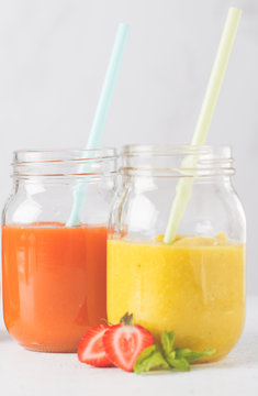 Multicolored fruit juices or smoothie in glass jars and ingredients, isolated on white background.