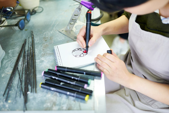 High angle close up of young female artist drawing sketch ready to create beautiful jewelry in glassworking studio