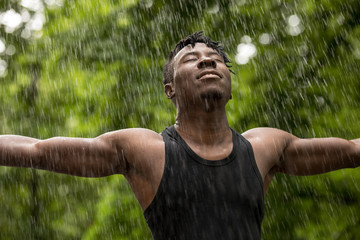 African man enjoying fresh summer rain while hands raised