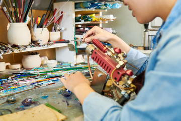 Crop shot of  Asian female artist working with glass, bending glass rod in modern workshop, copy space