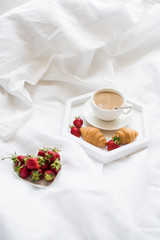 Early morning breakfast in bed, coffee and croissant with strawb