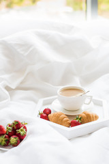 Early morning breakfast in bed, coffee and croissant with strawb