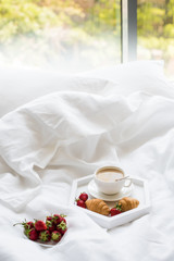 Early morning breakfast in bed, coffee and croissant with strawb
