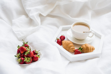 Early morning breakfast in bed, coffee and croissant with strawb