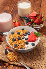 Bowl of homemade granola with yogurt and fresh berries on wooden background