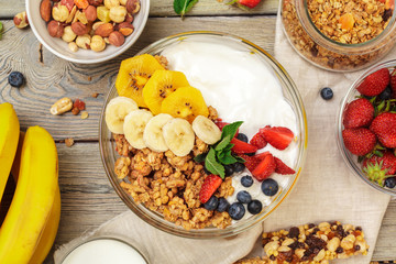 Bowl of homemade granola with yogurt and fresh berries on wooden background