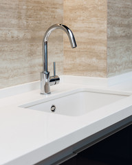 Detail of a white rectangular designer kitchen sink with chrome water tap against a tiled wall