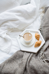 Cozy breakfast in bed, cup of coffee and croissants on white and