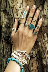Nahaufnahme der Frauenhand auf der Baumoberfläche mit viel Schmuck, Ringen und Armbändern im Boho-Stil © Coka