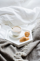 Fototapeta na wymiar Cozy breakfast in bed, cup of coffee and croissants on white and