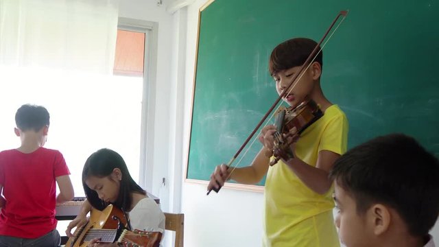 Young asian boy playing violin with friends in classroom