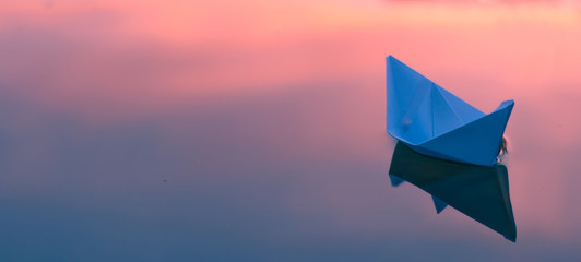 Paper origami boat floats on the surface of the water at sunset or dawn