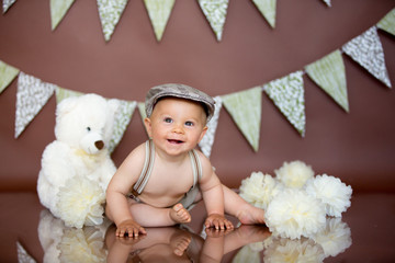 Little baby boy, celebrating his first birthday with smash cake party, studio isolated shot on brown