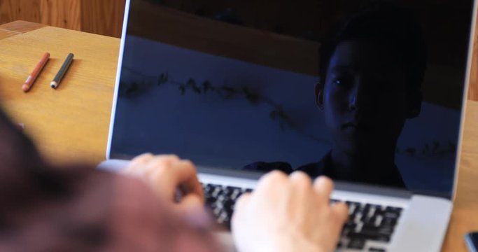 Reflective image on laptop screen of Asian young man working