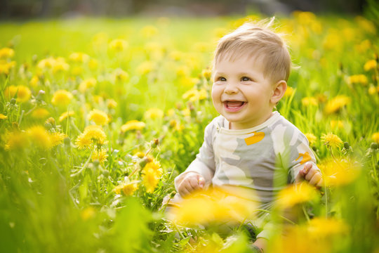 Concept: family values. Portrait of adorable innocent brown-eyed baby playing outdoor in the sunny dandelions field and making funny faces.