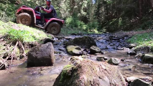 the guy is riding a quad bike through a stream in the forest