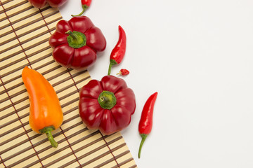 Several ripe sweet and hot peppers on a straw napkin on a white background