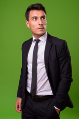 Young handsome Hispanic businessman against green background