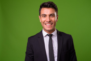 Young handsome Hispanic businessman against green background