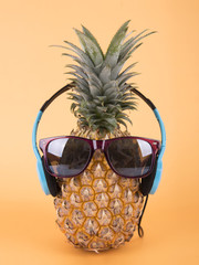 Pineapple with sunglasses and headphone on orange background. fruit summer concept.