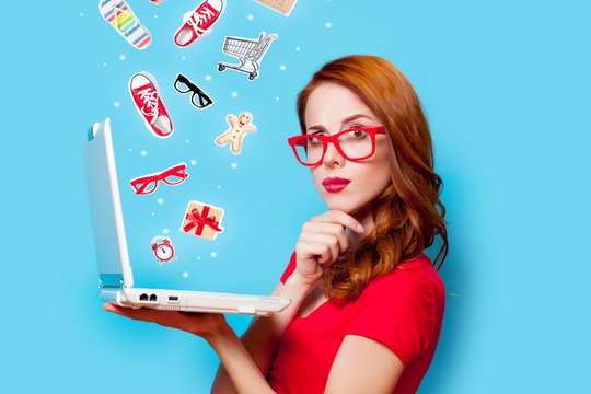Young beautfiul redhead girl in eyeglasses with laptop computer on blue background
