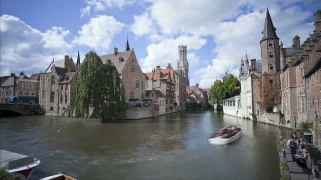 Waterfront buildings and pleasure craft with tourists in Flanders, canal buildings and bell tower the city of Bruges, Belgium, Europe, T/Lapse