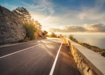 Mountain road at sunset in Europe. Landscape with rocks, sunny sky with clouds and beautiful asphalt road in the evening in summer. Colorful travel background. Highway in mountains. Transportation - Powered by Adobe