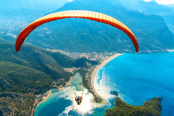 Paragliding in the sky. Paraglider tandem flying over the sea with blue water and mountains in...