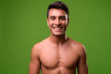 Young handsome Hispanic man shirtless against green background