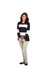 full length portrait of girl wearing striped blue and white jumper and jeans and holding a book. standing pose on white studio background