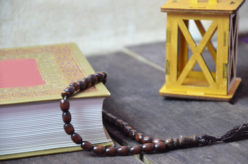 Quran, beads, and lantern on old wood with a beautiful sunrise as background. Ramadhan Concept.